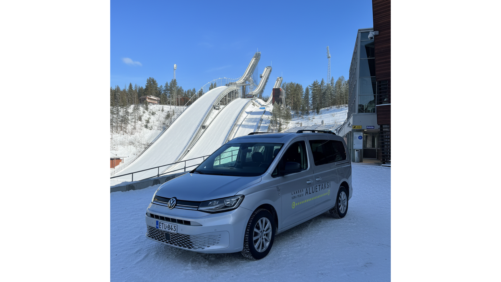 Taksi Wallin Oy:n tilataksi pys&auml;k&ouml;ityn&auml; Lahden ikonisten hyppyrim&auml;kien edustalle talvip&auml;iv&auml;n&auml;. Autossa on Lahden Aluetaksin teippaus.